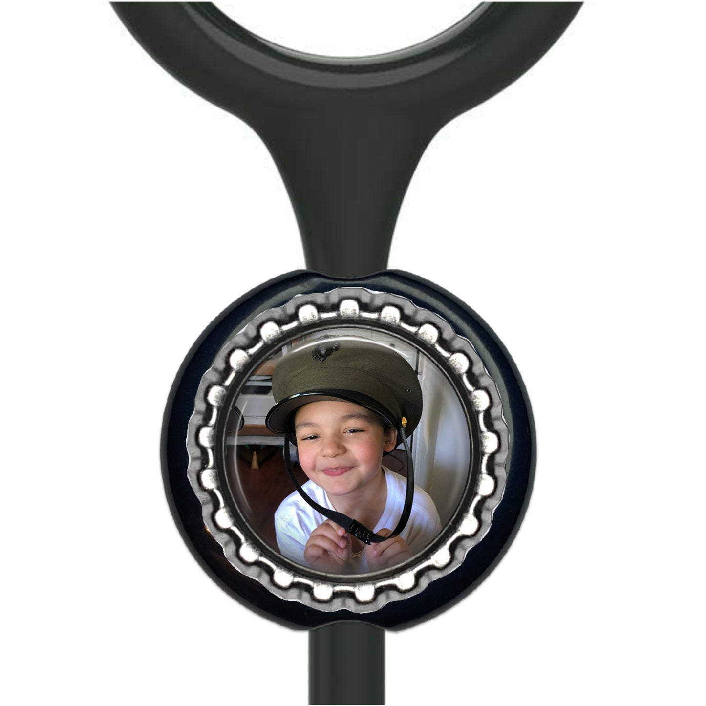 A young boy wearing a hat is smiling at the camera, with a black stethoscope charm featuring a circular photo of the boy attached to it.