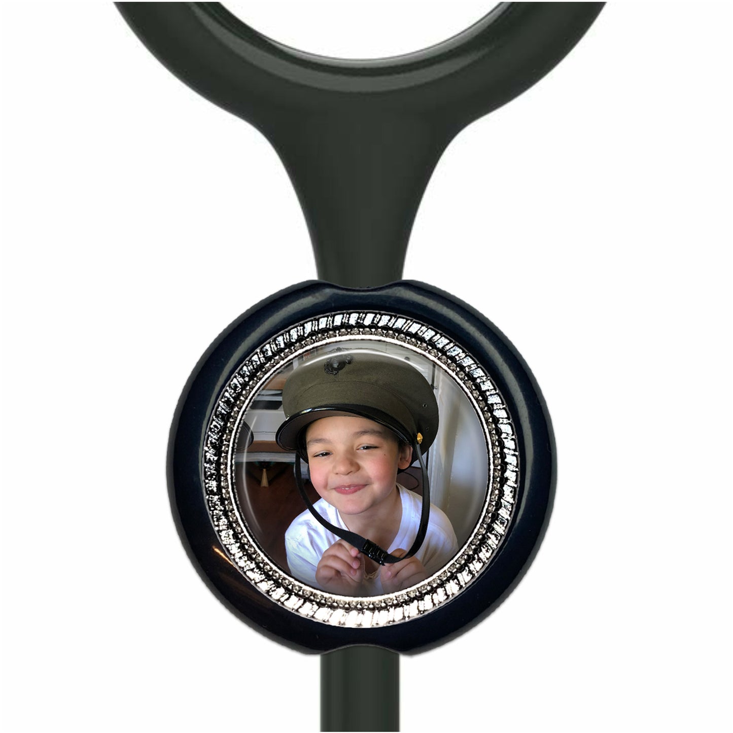 A young boy wearing a helmet is smiling at the camera, with a black stethoscope-style charm featuring a photo of the boy attached to it.