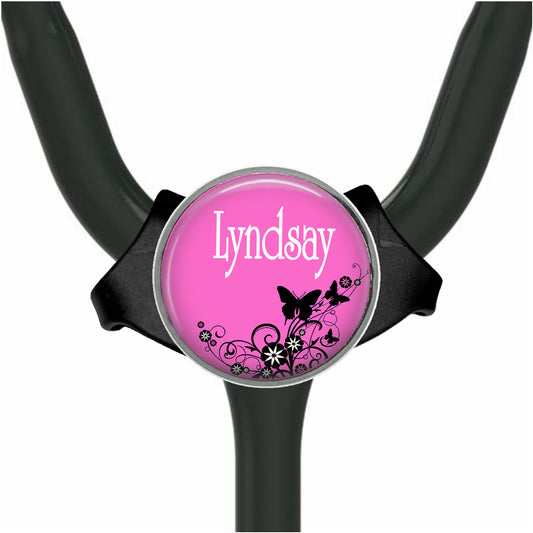 A pink circular badge with the name "Lyndsay" written on it, surrounded by black floral designs.