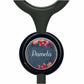 A black stethoscope with a circular charm featuring a floral design and the name "Pamela" written on it.