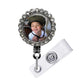A personalized badge with a photo of a smiling child inside a decorative frame, attached to a clear plastic holder.