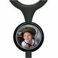 A young boy wearing a helmet is smiling at the camera, with a black stethoscope-like object featuring a circular mirror in the foreground.