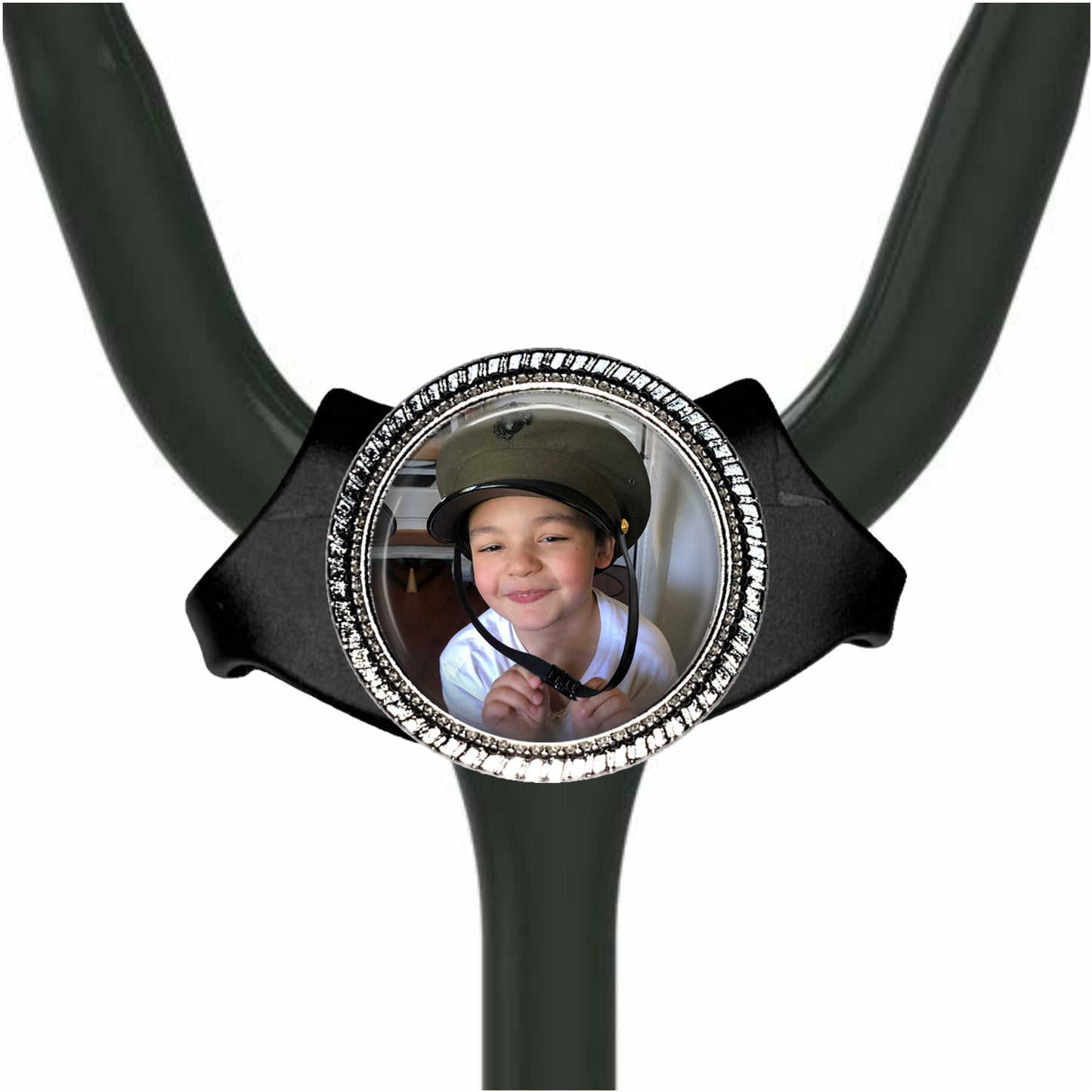 A young boy wearing a helmet is smiling at the camera, with a black stethoscope-style accessory featuring a circular frame with a photo of the boy inside.