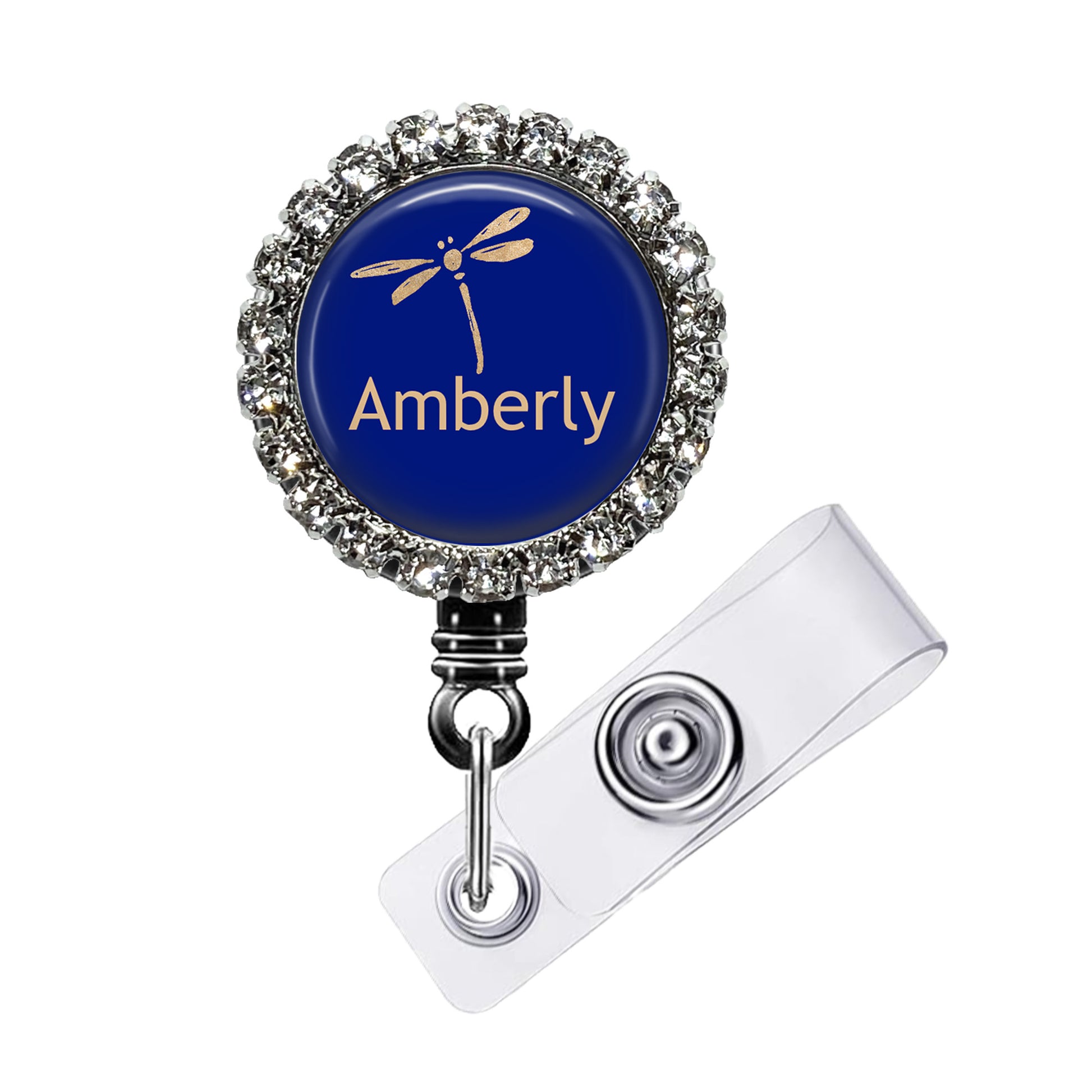 A blue badge with a silver rhinestone-encrusted frame, featuring a gold dragonfly design and the word "Amberly" written on it.