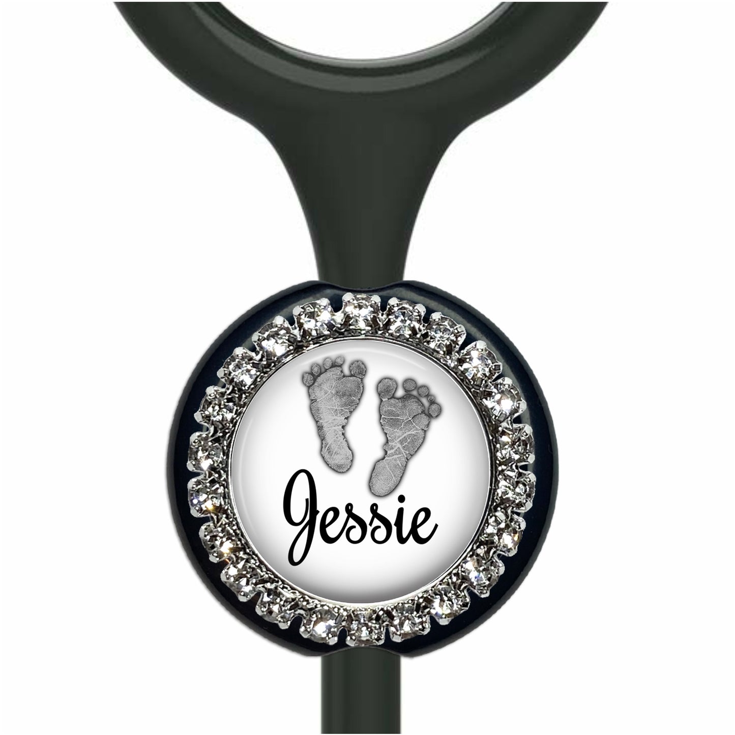 A personalized nameplate with a black background and a silver frame. The nameplate has a white circle with a black outline, and inside the circle, there is a black and white image of a baby's foot. The nameplate is personalized with the name "Jessie".