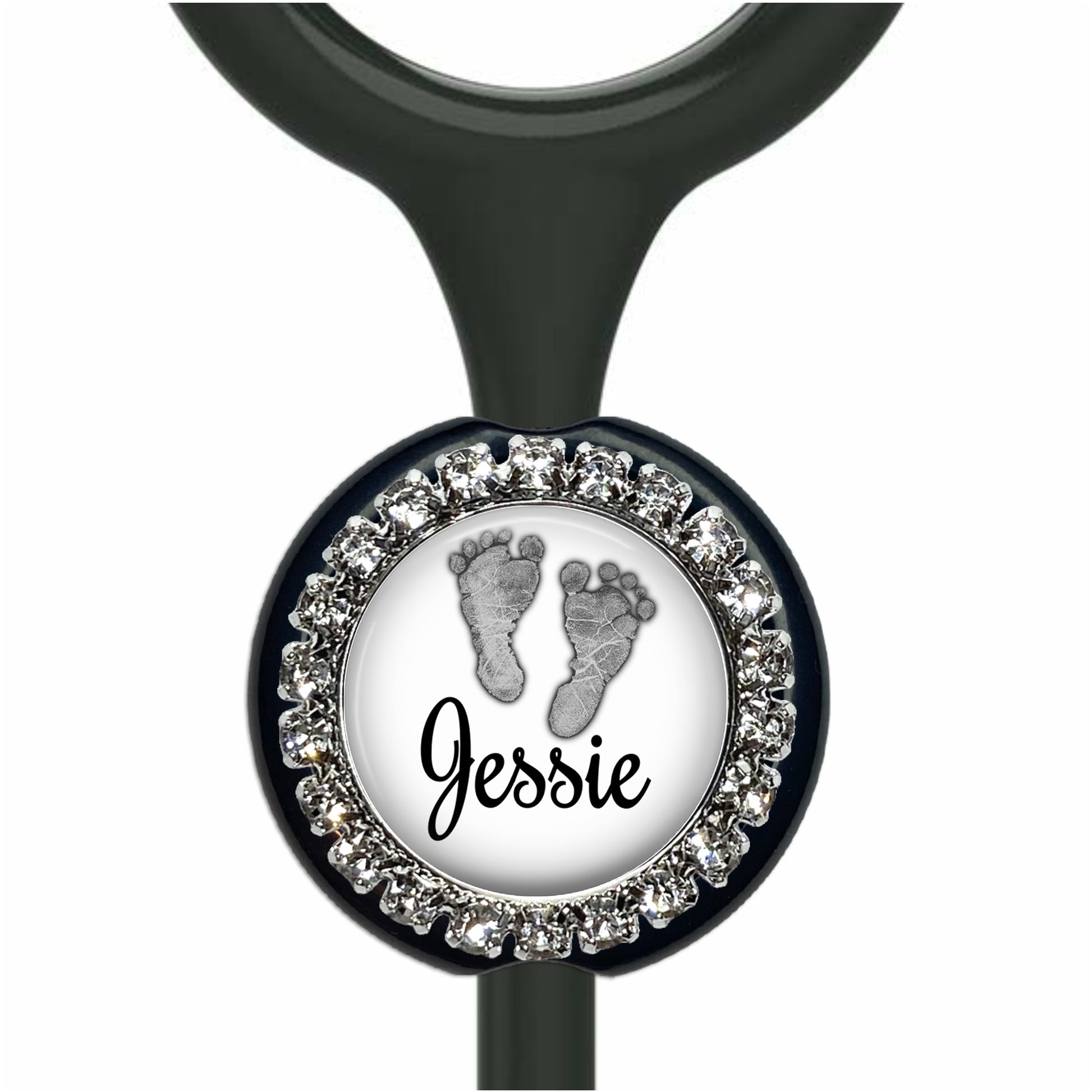 A personalized nameplate with a black background and a silver frame. The nameplate has a white circle with a black outline, and inside the circle, there is a black and white image of a baby's foot. The nameplate is personalized with the name "Jessie".