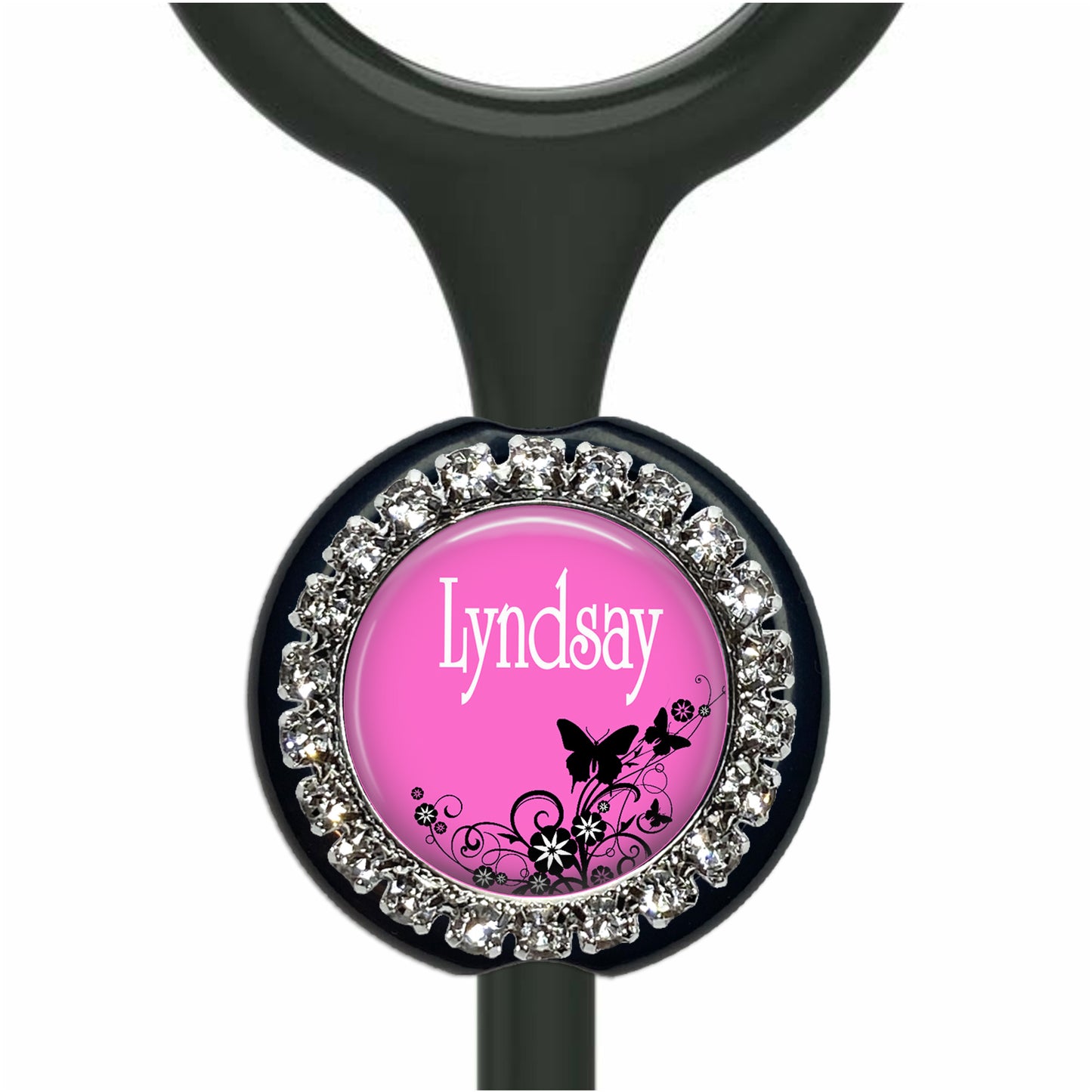 A pink-colored charm with a black and white floral design, and the name "Lyndsay" written on it. The charm is attached to a black object, possibly a stethoscope, with rhinestones or crystals around the edges.