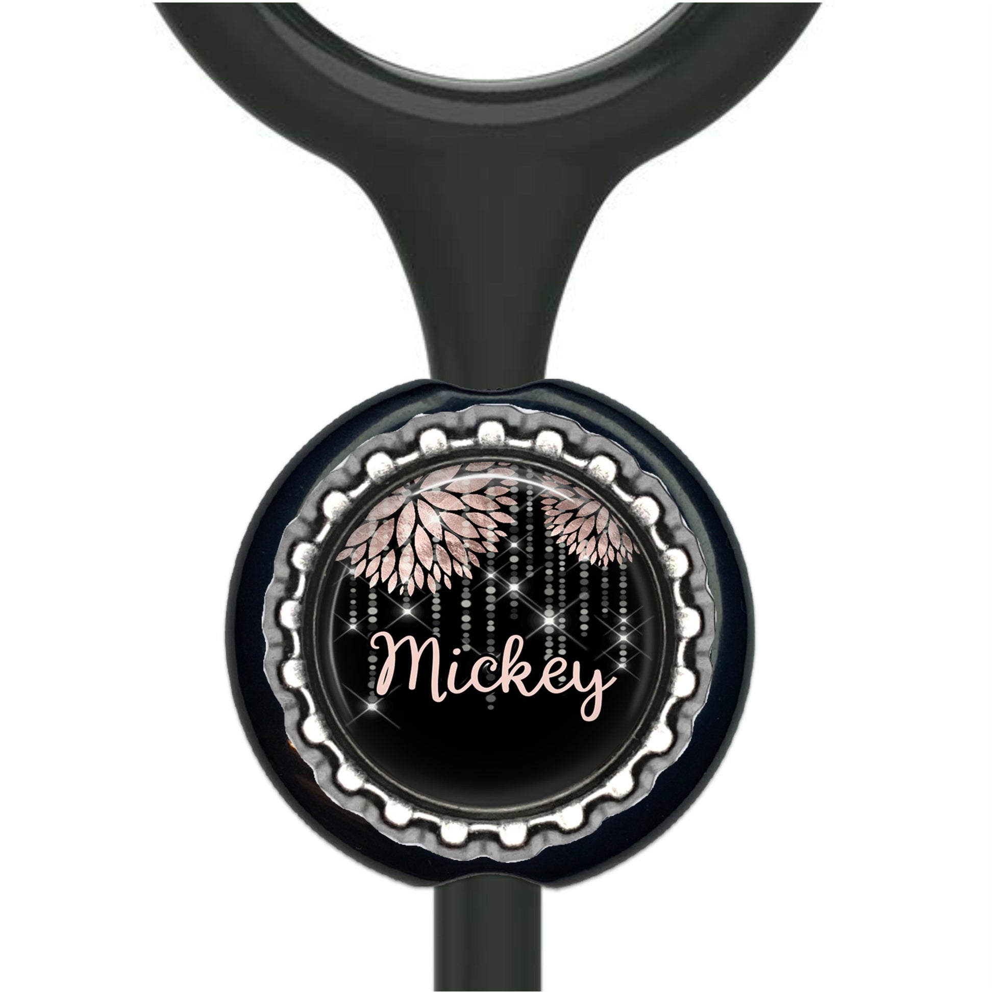 A black stethoscope with a round, black and silver button featuring a floral design and the name "Mickey" written on it.
