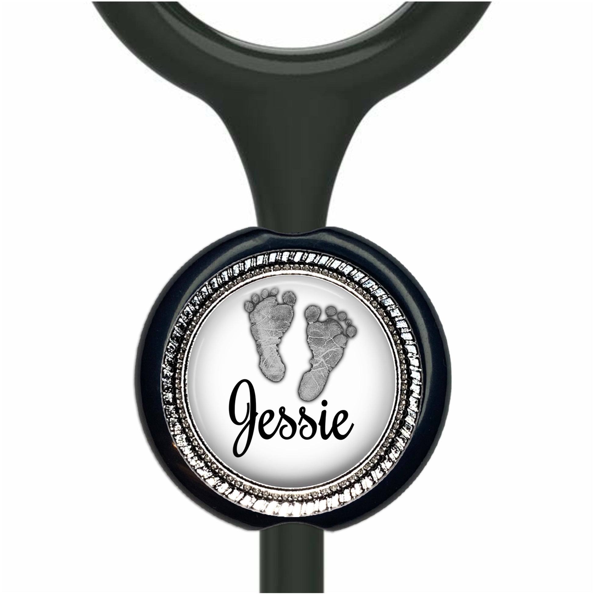 A black stethoscope with a personalized nameplate attached to it. The nameplate features a circular design with a black and white image of a baby's foot and the name "Jessie" written in cursive.